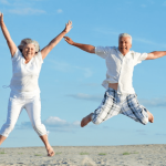 白人の老夫婦が浜辺で嬉しそうに手を上げてジャンプしている写真